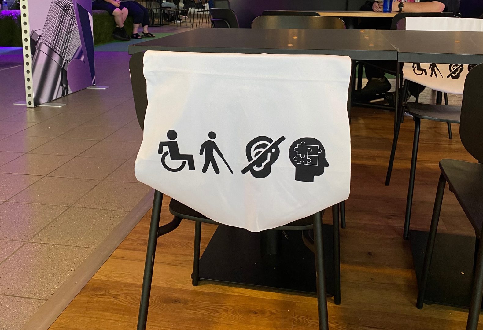Stoel met een hoes over de rugleuning met de symbolen voor 4 groepen beperkingen. De symbolen zijn een persoon in een rolstoel, een persoon met een taststok, een oor met een streep erdoor en een hoofd met puzzlestukjes erin