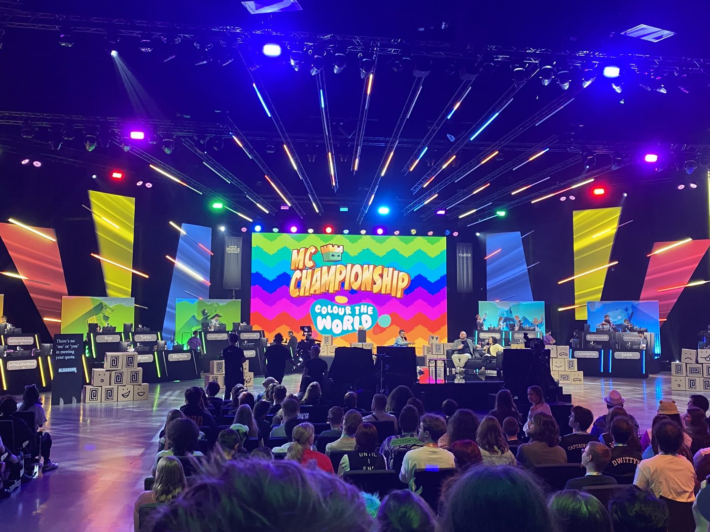 Foto van het hoofd podiu, met op het scherm regenboog kleuren als achtergrond met de tekst erover MC Championship Colour the World